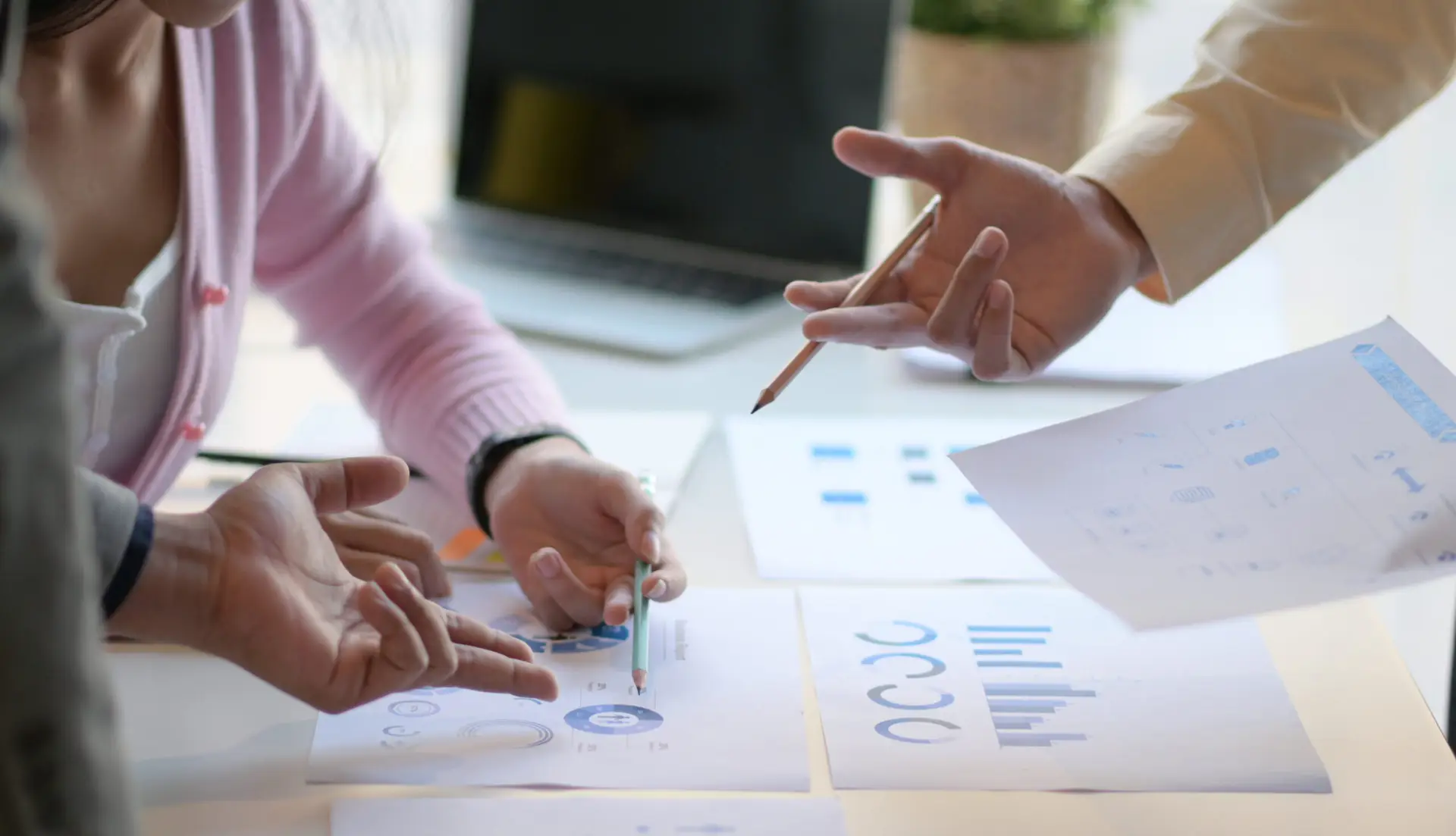 Three people in image pouring over papers with data on a table. You cannot see anyone's face or head