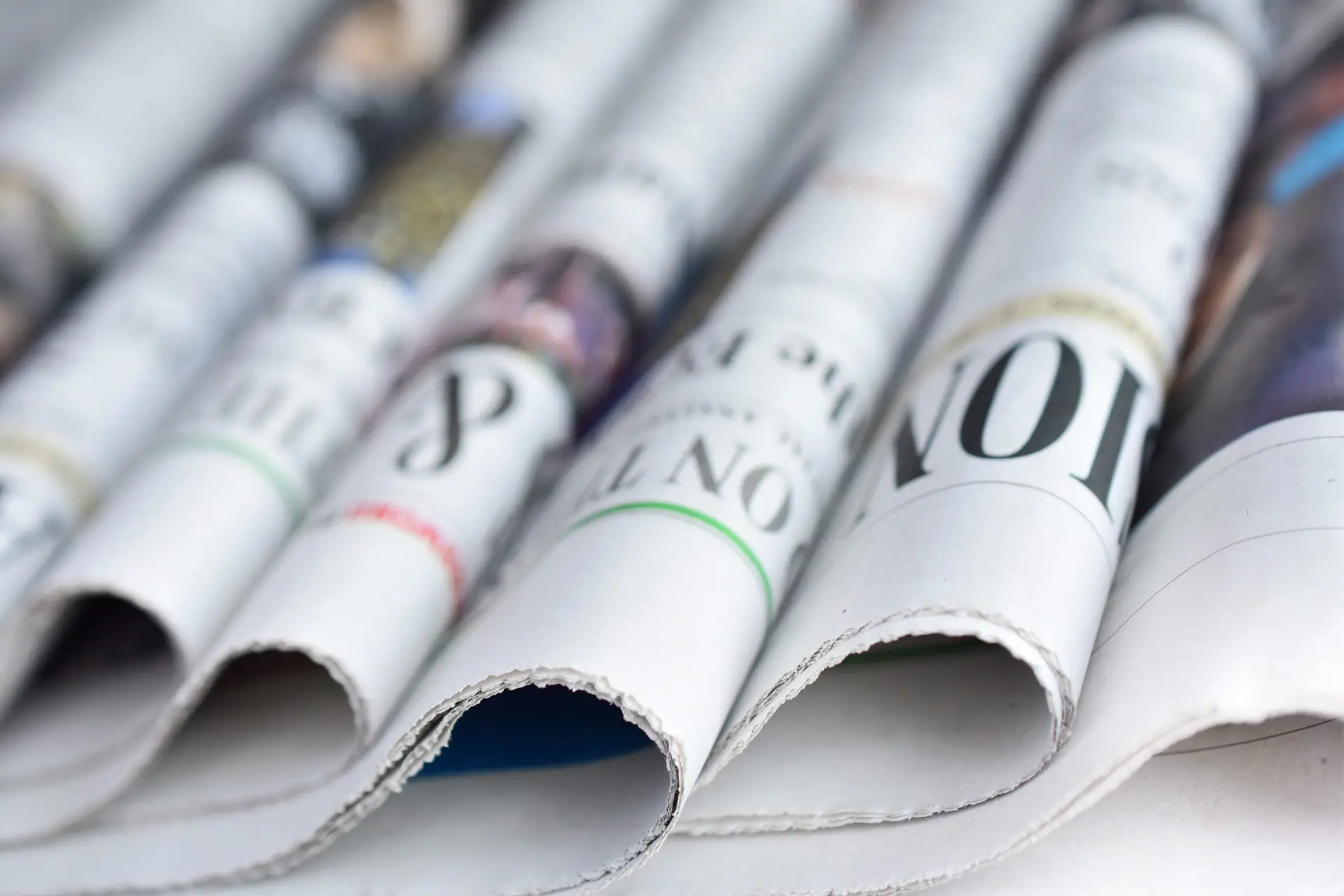 Seven newspapers rolled in half all lined up. You can't read the headlines, but the effect is of many headlines